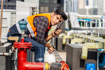 Male technical foreman inspection maintenance sitting on workshop site break relax time with talking on radio call with colleague about plumbing and electrical systems on the roof of a building