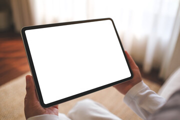 Mockup image of a woman holding digital tablet with blank desktop screen while sitting on a sofa at home