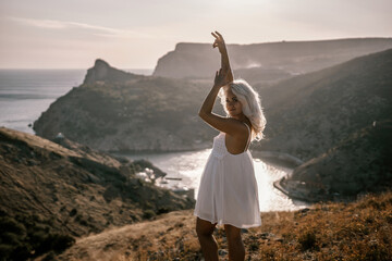 A woman stands on a hill overlooking a body of water. She is wearing a white dress and she is enjoying the view. - Powered by Adobe