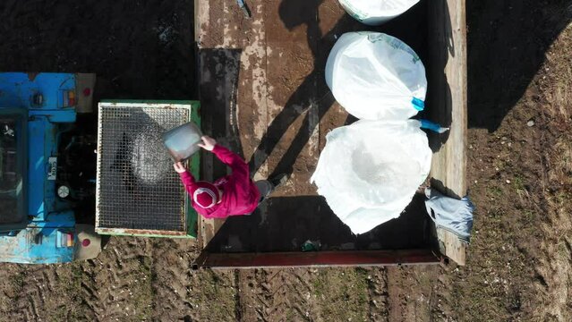 Above view farmer use metal bucket to fill up spreader with mineral fertilizer