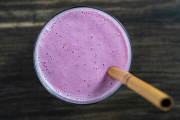 Raspberry banana smoothie with a bamboo straw on a wooden table, closeup, top view - 781852201