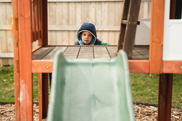 Little kid climbing on playground in backyard to go down slide