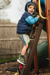 Young boy climbing up playground ladder while sticking his tongue out