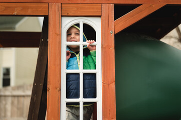 Happy young toddler boy smiling through backyard playground window