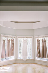 Wedding dress and bridesmaid dresses hanging in sunlit room