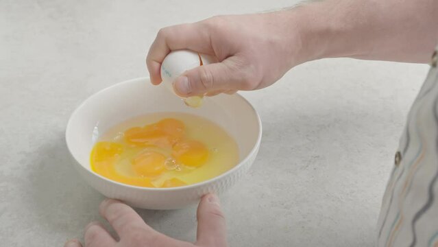 A man cracks a chicken egg into a plate, preparing to cook a dish. Perfect for culinary projects and tutorials.