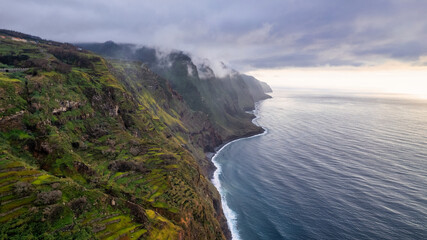 The cliff on Madeira rises above the azure ocean. The cliff is tall and steep, with an uneven and...