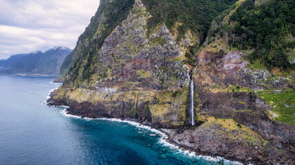 A waterfall cascading down a mountainside in Madeira, surrounded by green foliage and rocky...