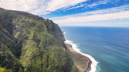Steep, green slopes of Madeira, covered with vegetation, descending to the blue ocean; fog envelops...