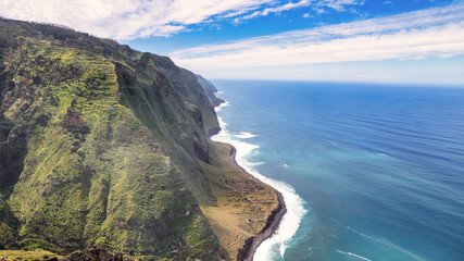 The cliff on Madeira rises above the azure ocean. The cliff is tall and steep, with an uneven and...
