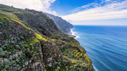 Steep, green slopes of Madeira, covered with vegetation, descending to the blue ocean; fog envelops...