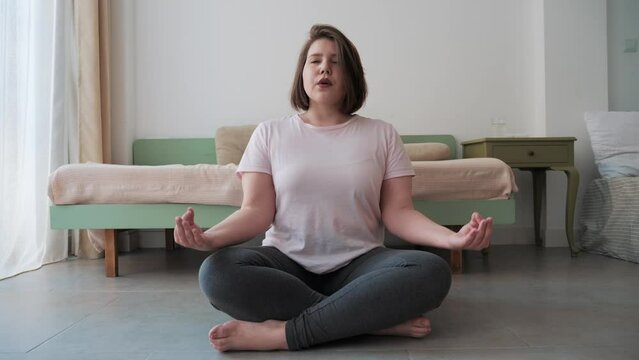 Woman sits cross legged on floor, deeply engaged in breathing exercise for relaxation and health. 