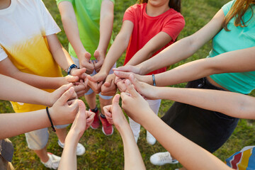 Top view portrait of a kids friends standing in a circle outdoors and showing thumbs up sign. Hands of boys and girls in summer casual clothes. Childhood, unity and friendship concept.