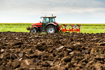 Tractor with plow attachment turns the soil in a vast, green farmland