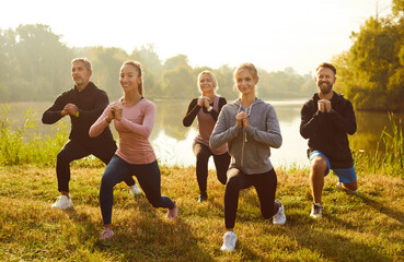 Active sporty people doing stretching exercising in nature. Happy smiling men and women in sportswear having sport workout in the park in the morning. Outdoors training and fitness concept. - obrazy, fototapety, plakaty