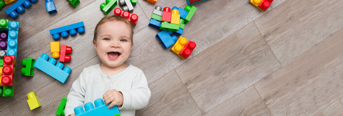 child baby playing with lots of colorful plastic blocks constructor on floor in the room. banner. copy space