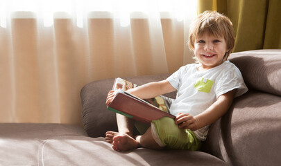 Child boy reading a book sitting  on the sofa. copy space