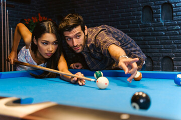 Young diversity group of people playing pool together with smile, enjoyment and fun. Young people spend time in billiards room at the nightclub. Men, women friends playing billiards. Nightlife concept - 781869204