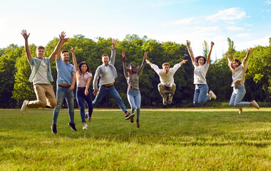 Naklejka premium Group of diverse people having fun in summer park. Several happy carefree excited cheerful joyful young multiracial friends jumping together on grassy lawn in green park under blue sky