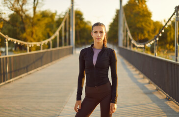Portrait of a young female athlete during an outdoor fitness workout. Beautiful slim woman in black...
