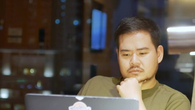 asian man while working on laptop in night time shift