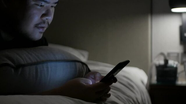 asian man while chatting on mobile phone and lay on the bed in bed room in night time