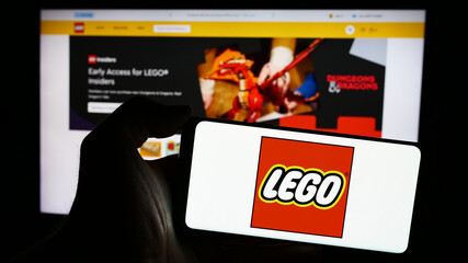 Fototapeta premium Stuttgart, Germany - 04-02-2024: Person holding mobile phone with logo of Danish construction toy company LEGO AS in front of business web page. Focus on phone display.