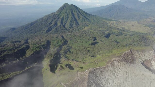 A mountain range with a volcano in the background. The mountain is covered in trees and the volcano is covered in snow