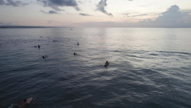 A group of people are surfing in the ocean. The water is calm and the sky is cloudy