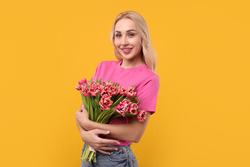 Happy young woman with beautiful bouquet on orange background