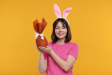 Easter celebration. Happy woman with bunny ears and wrapped egg on orange background
