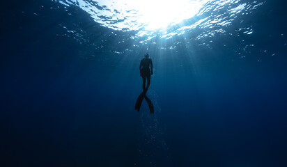 Freediver Swimming in Deep Sea With Sunrays. - obrazy, fototapety, plakaty