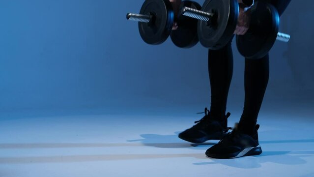 Women's hands lift heavy dumbbells from the floor. Sports model in the studio. Close-up.
