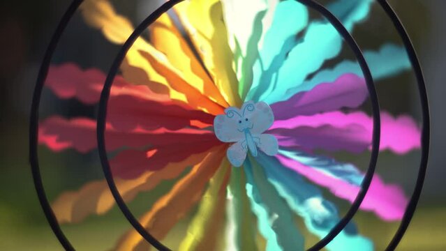 Colorful rainbow wind spinner spinning outdoors in sunny garden, close-up.