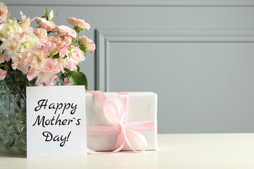 Happy Mother's Day greeting card, gift box and bouquet of beautiful flowers on white wooden table