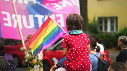 Little kid sit mother shoulder. Gay protest against no homophobia. Family walk lgbt pride parade. Child watch lesbian strike. Bi parent show us csd fest daughter. Peaceful rally Girl hold rainbow flag