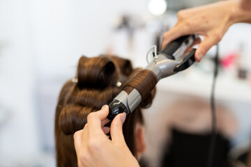 The hairdresser curls the model's hair. Curling iron for curling hair close-up.