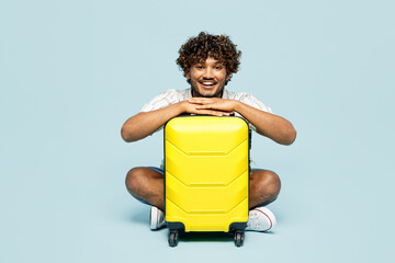 Full body fun traveler Indian man wear white casual clothes sit holding bag isolated on plain blue background. Tourist travel abroad in free spare time rest getaway. Air flight trip journey concept. - 781901827