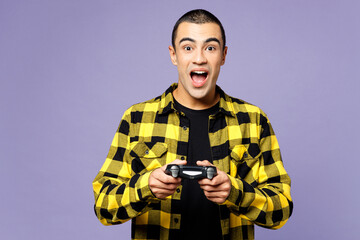 Young surprised shocked middle eastern man wear yellow shirt casual clothes hold in hand play pc game with joystick console isolated on plain pastel light purple background studio. Lifestyle concept. © ViDi Studio