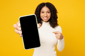 Little fun kid teen girl of African American ethnicity wear white casual clothes hold use point on blank screen area mobile cell phone isolated on plain yellow background. Childhood lifestyle concept. - 781902819