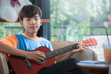 Asian boy is relaxing and playing ukulele at the corner of his home during the weekend, happiness...