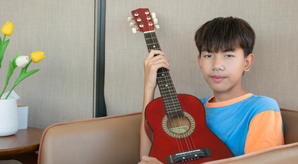 Asian boy is relaxing and playing ukulele at the corner of his home during the weekend, happiness of children with popular instruments concept.