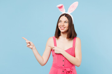 Young smiling woman she wear pink casual clothes rabbit bunny ears point index finger aside on area...