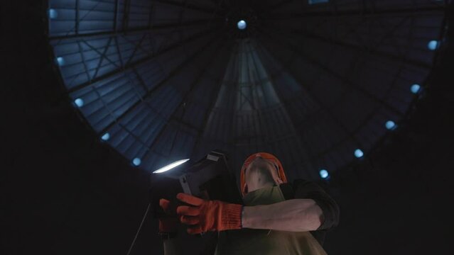 Male worker in safety helmet with flashlight in hands inside storage tank. Inside the grain silo.