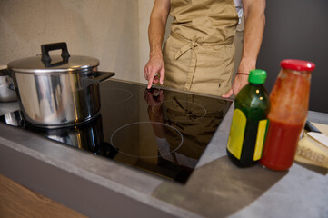 Close-up view of a man holding hand on the black glass surface of an electric or induction stove,...