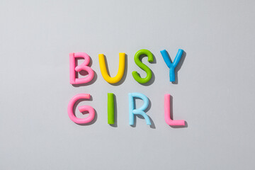 The word "busy girl" from colored plasticine on a gray background.