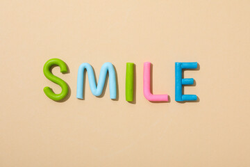 The word: "smile" laid out from colored plasticine on a peach background.
