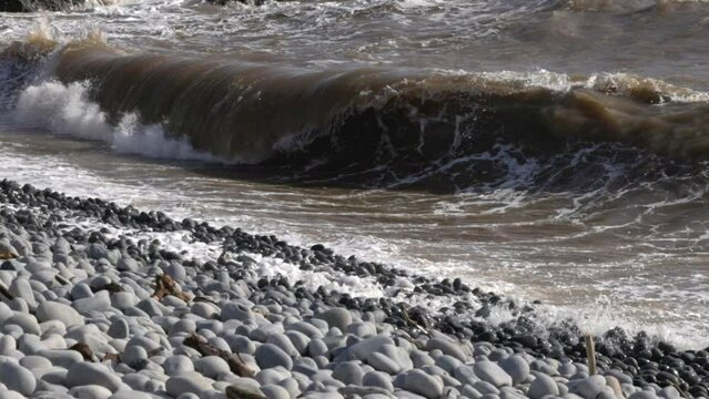 Slow motion shot of dirty water waves rolling and crashing onto cobble beach