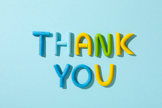 The word "thank you" from colored plasticine on a blue background.