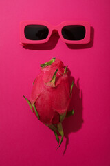 One whole dragon fruit and sunglasses on pink background, top view
